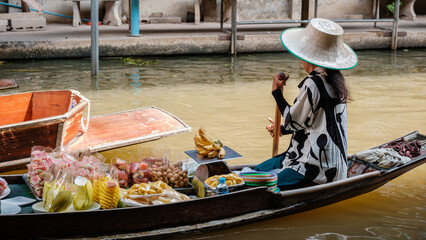 Obraz premium Explore the dynamic atmosphere of the Damnoen Saduak Floating Market in Thailand. Vendors sell fresh fruits and local delicacies from their boats while colorful scenery unfolds on the water.