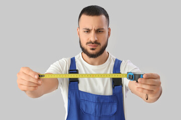 Young male construction worker with measuring tape on grey background