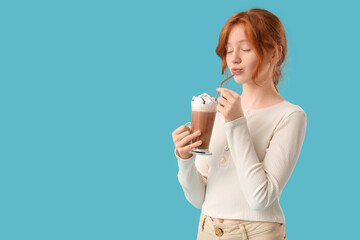 Teenage redhead girl drinking sweet cocoa on blue background