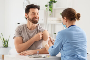 Obraz premium Young man with doctor applying medical patch after vaccination in clinic
