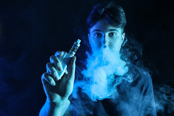 Handsome young man smoking electronic cigarette on black background, closeup