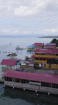 Vertical aerial view showcasing colorful buildings and boats along the waterfront of Bastimentos Island, Bocas del Toro, Panama.