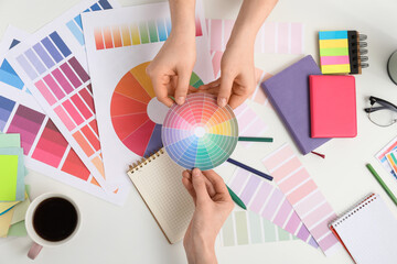 Female graphic designers holding color palette on white background, top view