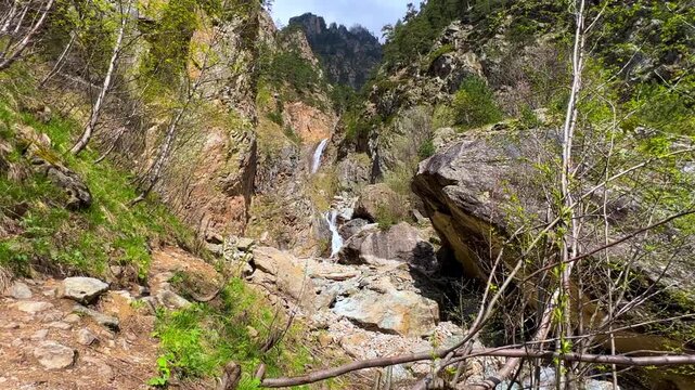 Shagatsikomdon Waterfall, in the spring in the Caucasus Mountains. Mountain landscape. Waterfall in the Tsey Gorge. North Ossetia-Alania, Russia. A multi-stage 15-meter waterfall in the sunlight. 4К
