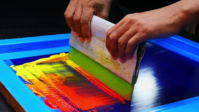 Colorful screen printing workshop scene where red, orange, and yellow inks merge across the mesh screen, illustrating the intricate manual process of creating bold and dynamic gradient prints by hand
