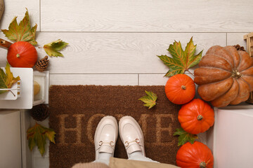 Woman with autumn leaves and pumpkins on doormat in hallway, top view