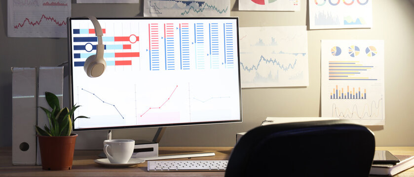 Data scientist's workplace with computer and diagrams in dark office - Powered by Adobe