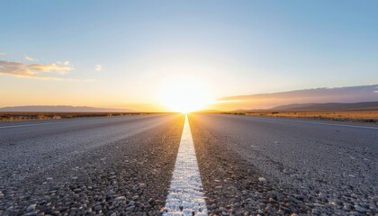 Sunrise over a deserted road with a white line down the center, set against a clear blue sky with clouds, in a serene and peaceful natural landscape.