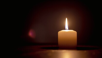 A single lit candle with a warm glow against a dark background, casting a subtle shadow.