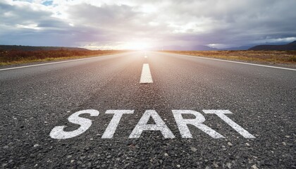 Asphalt road with 'START' painted on it stretching into the distance towards a bright sunrise or sunset with clouds