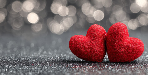 Obraz premium Two red hearts on sparkling silver background with glitter create romantic and festive atmosphere full of warmth and love