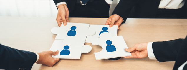 Hands assemble puzzle pieces featuring person icons, symbolizing networking and collaboration in a...