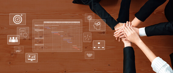 A top-down view of hands stacking in collaboration, featuring a digital Gantt chart and business icons, symbolizing teamwork and strategic planning in a modern office setting. Trope