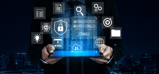 A businessman holds a futuristic tablet displaying security and data management icons against a city skyline backdrop at night, representing modern technology concepts. Gantry