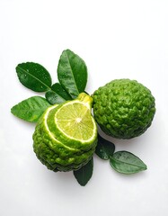 Overhead shot displays two textured, green citrus fruits with cut sections revealing the juicy interior. Vibrant green leaves complete the composition