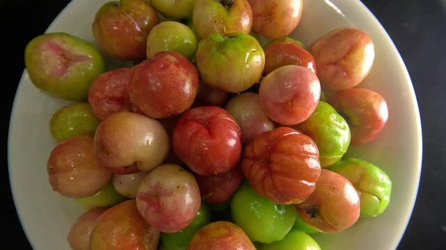 Close-up shot of fresh acerola cherries arranged on a white plate.