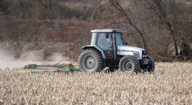 Sellersville, Pennsylvania, U.S - Dec 13, 2025 - White tractor plows harvested corn field, preparing soil for next planting season in late fall.