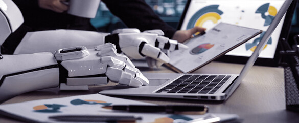 A modern office scene showcasing robotic hands analyzing data charts on a laptop, illustrating the fusion of technology and productivity in business environments.Noogenesis