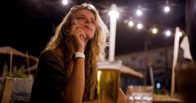 Enjoying a cigarette and a cold beer at a cozy restaurant on a warm evening under twinkling lights