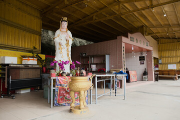 a religious shrine featuring a white statue of guanyin (goddess of mercy) with an incense burner, located within a natural cave structure, heping island park, Keelung, taiwan.