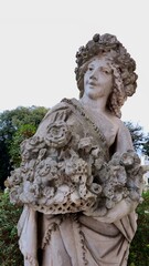 Rome, Italy - 12 January 2025. A statue in Villa Borghese shows a woman with flowered hair holding an overflowing bouquet of carved blooms in a garden setting.