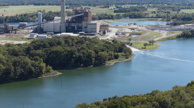 River bend with power facilities and wooded banks bordering calm water, aerial establishing tracking left tilt up