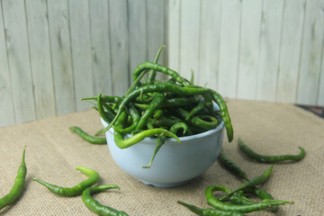 A beautiful composition featuring fresh green curly chilies (Capsicum annuum) piled in a light blue...