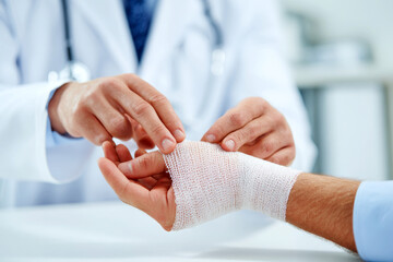 Professional medical person at the hospital bandaging the hand with a medical bandage for a patient.
