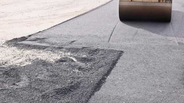 Heavy machinery is actively smoothing asphalt on city road preparing for new surface work.