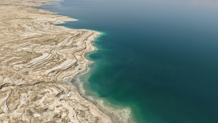 Aerial view of the Dead Sea in Israel captured from above, showcasing dramatic salt formations, turquoise water, and surrounding desert landscape