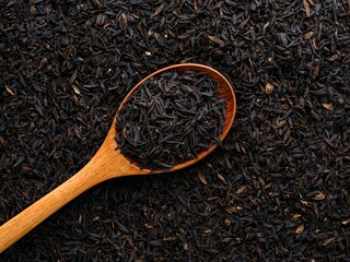 Wooden spoon with loose black tea leaves on dark textured background, close-up ingredient concept.