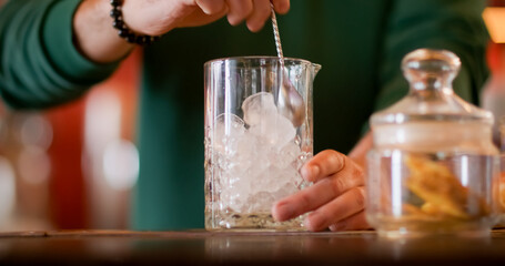 Stirring ice. Cocktail making. Barkeeper hand mixing frozen cubes ingredients in tall glass with metal spoon. Cooling refreshing drink.