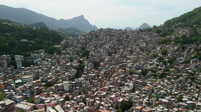 An aerial pull back reveals the dense urban layout of Rocinha favela nestled between steep forested hillsides and surrounding mountains
