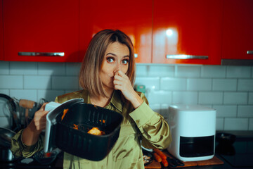 Woman Covering Her Nose Holding Dirty Air fryer Cooking Basket. Unhappy lady finding food residue that smells bad in her cooking appliance 