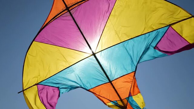 Vibrant Colorful Diamond Kite Soaring Against a Bright Sunny Blue Sky with Sun Peeking Through Fabric