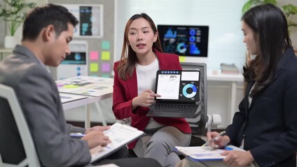 A woman is showing a laptop to two other people. The laptop is displaying a pie chart - Powered by Adobe