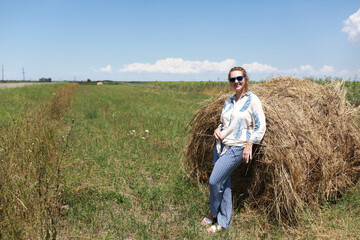 Caucasian woman in blue sunglasses relaxing by hay bale in field