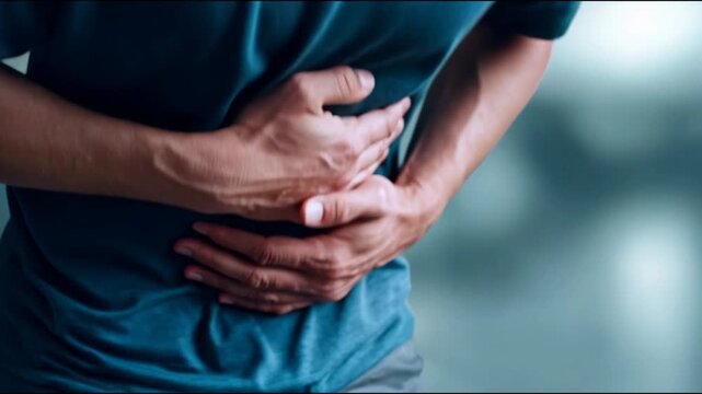 Young man holding his stomach in agonizing pain due to indigestion, appendicitis, or gastritis