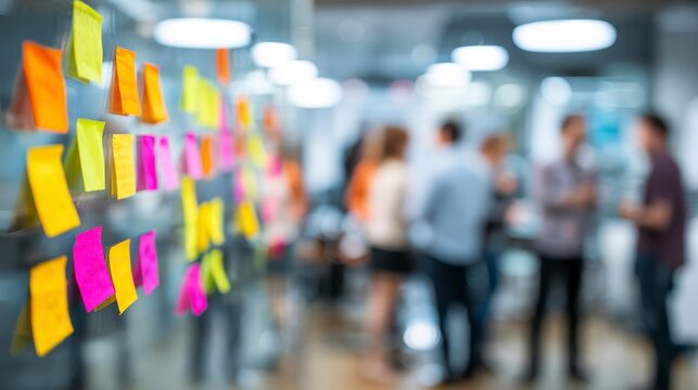 Focus on colorful sticky notes on a glass wall in an office, with blurred people in the background, a modern workspace