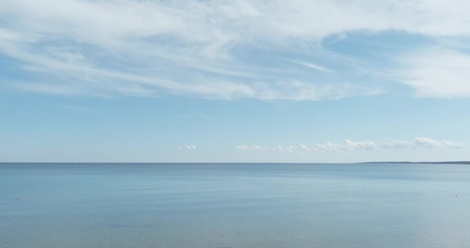 Aerial view of scenic view of a calm sea under a light blue sky with white clouds. The water is placid, reflecting the sky above, and a distant coastline is visible on the horizon, Hiiumaa, Estonia.
