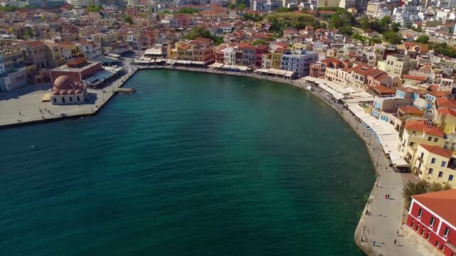 Cinematic aerial footage of Chania's Venetian Harbour with sightseers wandering along colourful buildings on Cretan Sea waterfront - Crete, Greece