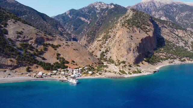 Drone panning round view of Agia Roumeli and end of Samaria Gorge with White Mountains towering above - Southern Crete, Greece