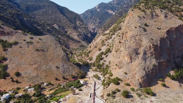 Aerial backwards reveal of Samaria Gorge, White Mountains and Libyan Sea at the coastal village of Agia Roumeli on Southern Crete
