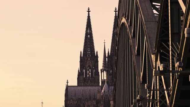 The contrast between the delicate, twin spires of the Gothic Cologne Cathedral (K&ouml;lner Dom) and the massive, industrial steel arches of the Hohenzollern Bridge.