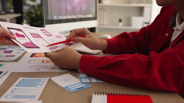 Excellent startup company employee presenting user interface prototype for mobile application to smart co-worker in office workspace. UX UI designer explain function of icon design on paper. Synergic