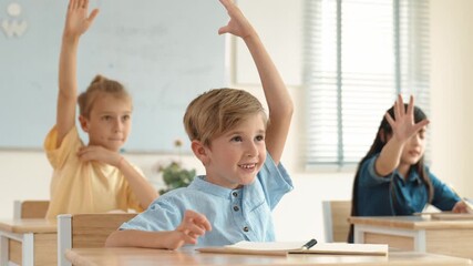 Caucasian boy raising hand for asking and answering teacher surrounded by diverse children studying at classroom. Happy student working together, voting, volunteering, calling instructor. Pedagogy. - Powered by Adobe
