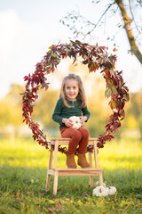 Fr&ouml;hliches M&auml;dchen sitzt auf einer Leiter in herbstlicher Naturkulisse mit Bl&auml;tterkranz und wei&szlig;en K&uuml;rbissen