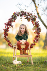 Lachendes M&auml;dchen sitzt auf einer Leiter in herbstlicher Naturkulisse mit Bl&auml;tterkranz und wei&szlig;en K&uuml;rbissen