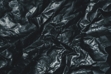 Dark crumpled plastic surface with glossy folds, abstract texture background for industrial, grunge, dramatic and modern design concepts