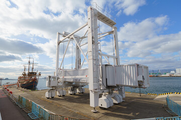 Large white self-propelled boarding ramp at Port of Osaka, Tempozan Wharf. Mobile gangway for cruise ships with the Santa Maria sightseeing vessel in the background. Industrial port infrastructure.